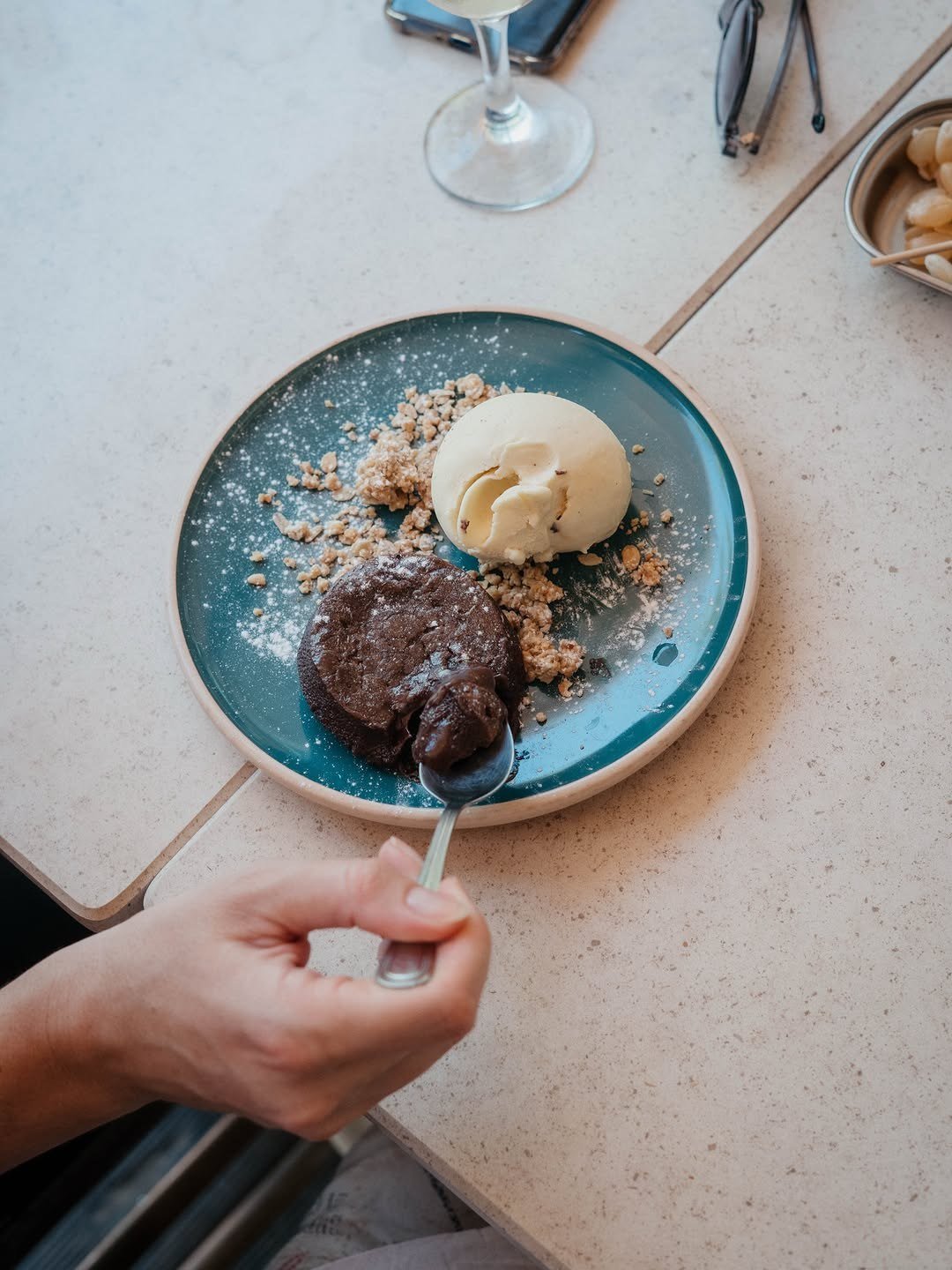 Prato azul com uma sobremesa de chocolate, uma bola de gelado de nata e migalhas de bolacha